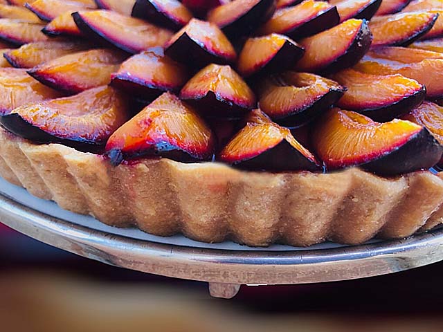 Tarte aux prunes en cuisson avec crème pâtissière vanillée et pâte dorée