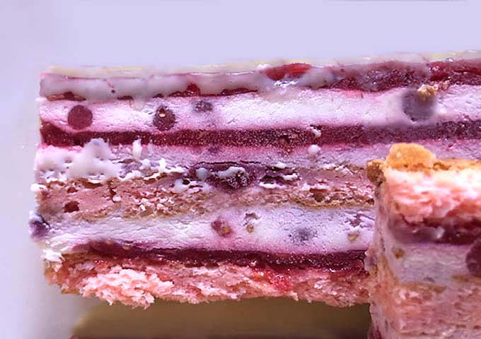 Coupe d’un entremets framboise litchi révélant les couches de biscuit pâte à choux, compotée de framboises et mousse fruitée